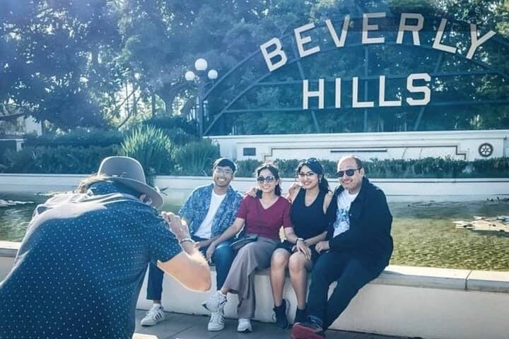 A photographer crouching to take a picture of four guests in front of the Beverly Hills sign