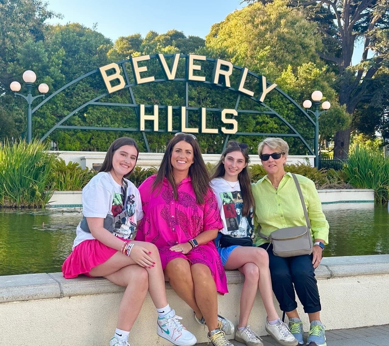 Four women sitting on the ledge in front of the Beverly Hills sign and its reflecting pool