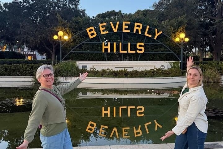 Two women posing on either side of the Beverly Hills sign, reflected in the pool