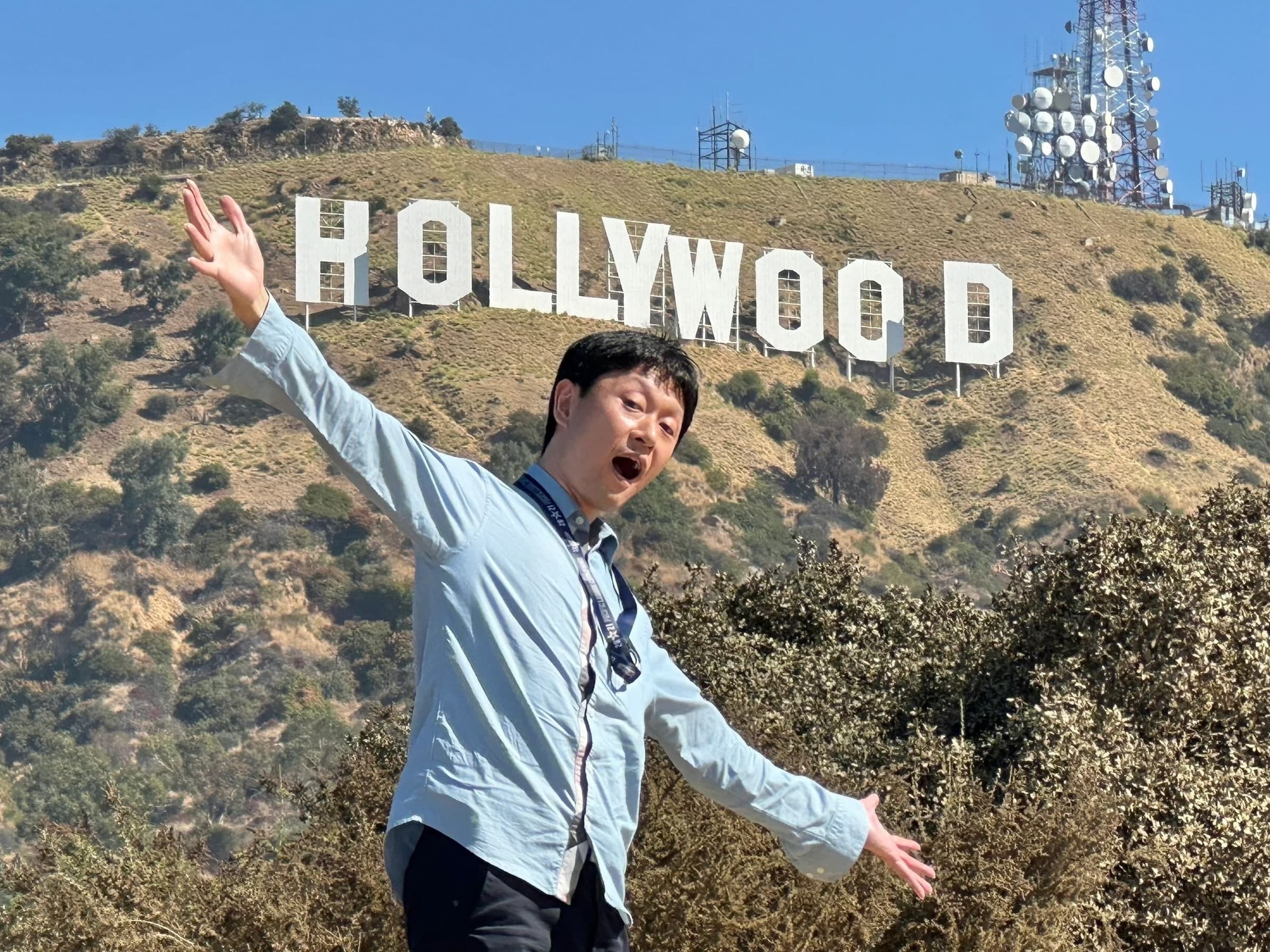 A man with his arms spread wide, the Hollywood Sign large behind him