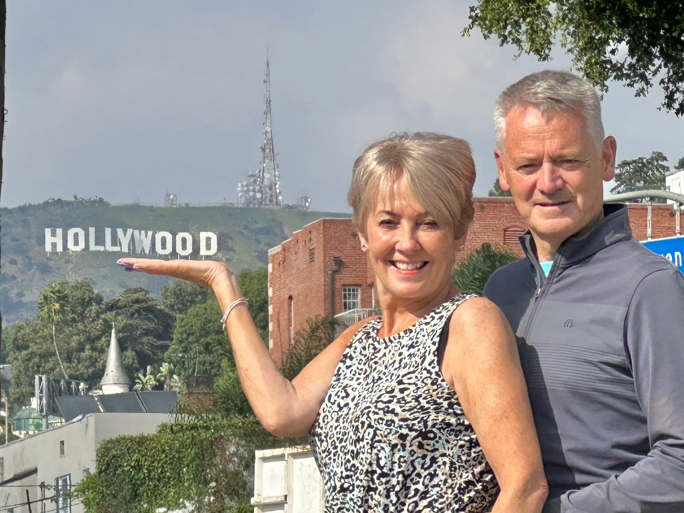 A couple posing so the Hollywood Sign appears to rest on her open hand