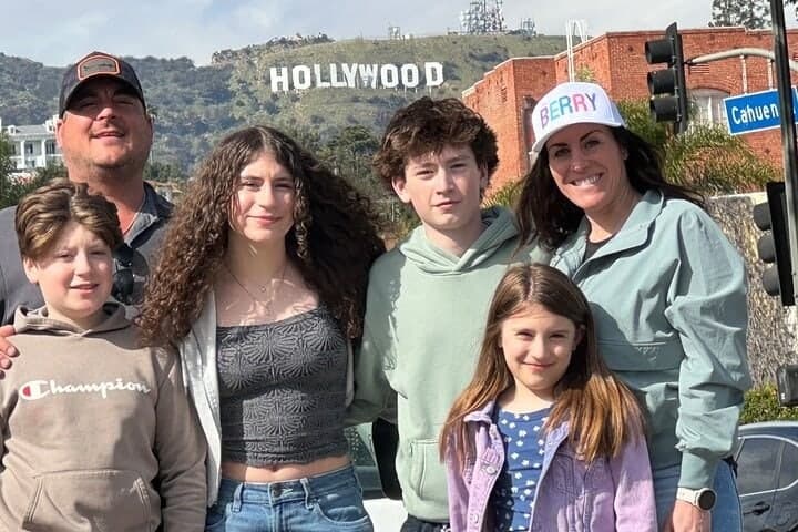 A family of five smiling with the Hollywood Sign in the background