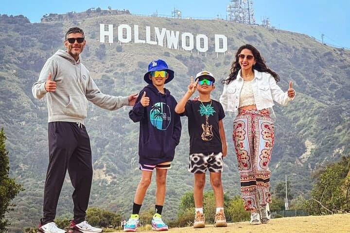 A family of four posing on a hillside path with the Hollywood Sign above