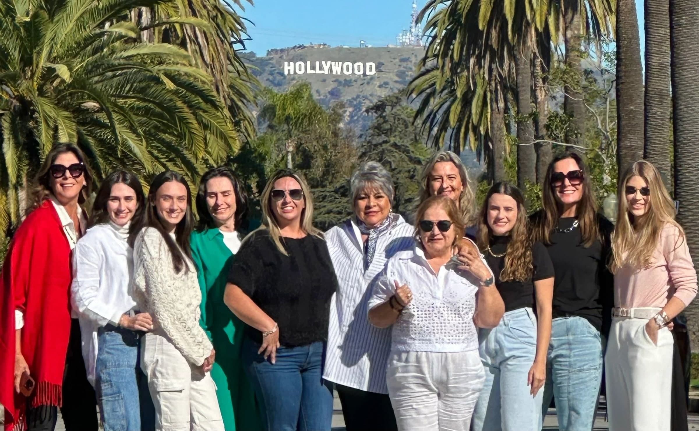 A large group of guests lined up under palm trees with the Hollywood Sign in the distance