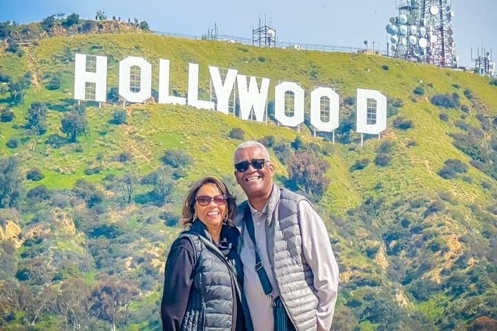 A couple standing close with the Hollywood Sign on green hills behind them