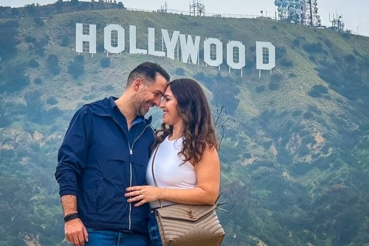 A couple leaning their heads together with the Hollywood Sign behind them
