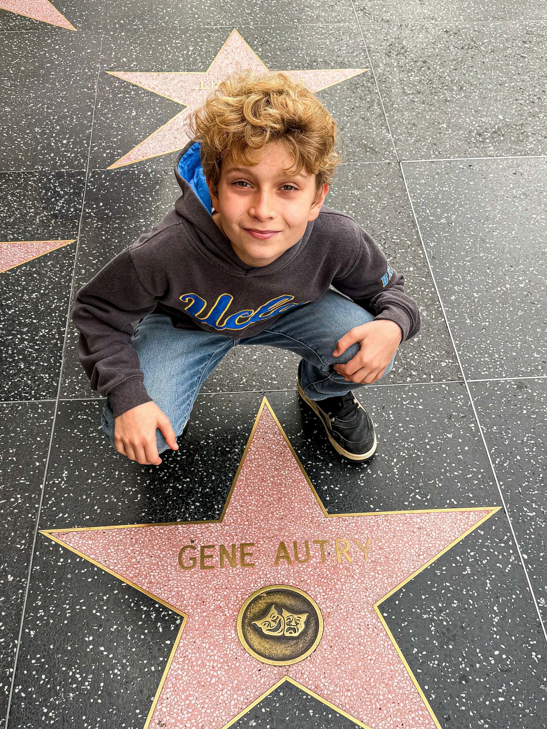 A boy crouching beside Gene Autry's star on the Hollywood Walk of Fame
